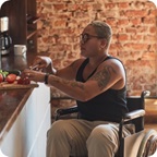 Person in a wheelchair sits in their kitchen and cuts vegetables. 